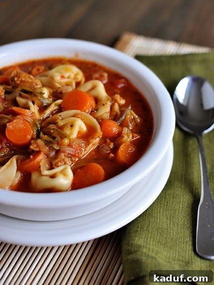 A white bowl with tortellini, sausage and veggie soup.