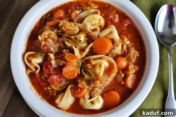 Top view of a sausage tortellini and veggie soup in a white bowl.