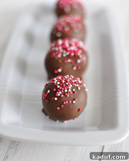 Fudgy No-Bake Brownie Truffles 4 An array of beautifully decorated brownie truffles, some generously covered in colorful sprinkles, others simply dipped in glossy chocolate, arranged in a white rectangular dish.