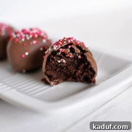 A close-up image of a single, perfectly formed brownie batter truffle, showcasing its smooth chocolate coating and sprinkle topping.