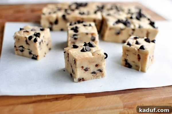 Ultimate Chocolate Chip Cookie Dough Fudge 3 A closer look at small, perfectly portioned squares of chocolate chip cookie dough fudge, freshly cut from a larger slab on parchment paper, ready to be served and enjoyed, emphasizing its rich texture and mini chocolate chips.