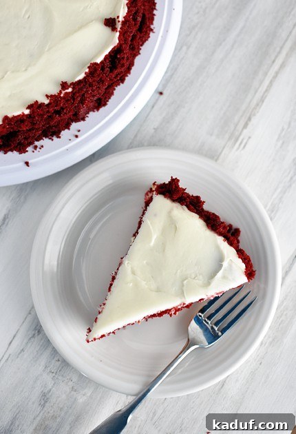 Red Velvet Cheesecake Dream 3 Top-down view of a single slice of Red Velvet Cheesecake Cake, frosted and ready to eat, on a white plate.