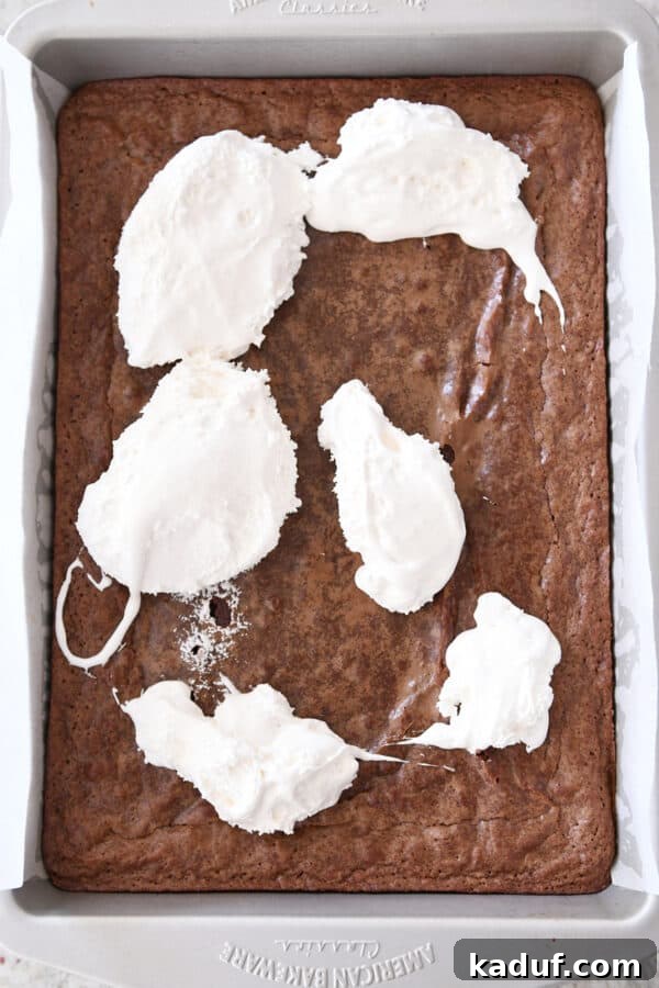 Ultimate Crunch Brownies 6 Marshmallow cream being dolloped in generous spoonfuls across the top of a warm pan of freshly baked brownies.
