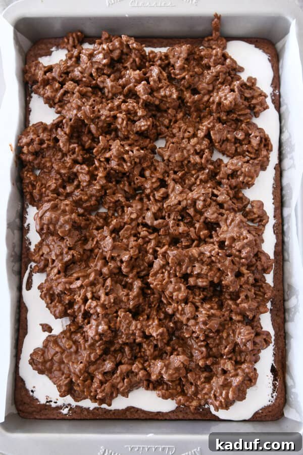 Ultimate Crunch Brownies 9 Carefully spreading the crispy peanut butter chocolate topping over the soft marshmallow cream layer on the brownies using an offset spatula.