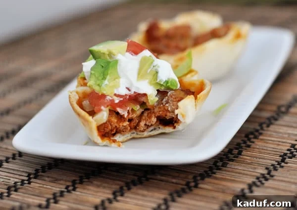 Tiny Taco Treats 3 A perfectly baked mini taco cup with a bite taken out, revealing the savory meat filling and crispy tortilla shell on a white platter.
