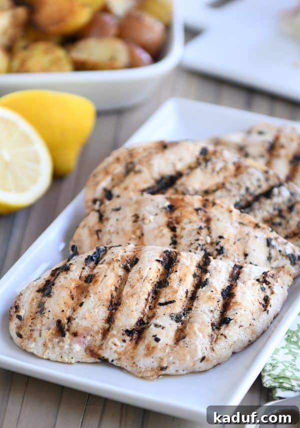 Several perfectly grilled lemon garlic chicken breasts arranged on a white platter, garnished with fresh lemon slices and parsley.