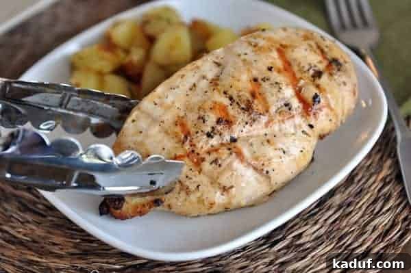 A perfectly cooked grilled chicken breast being lifted with tongs from a white plate, showcasing its golden-brown char marks.