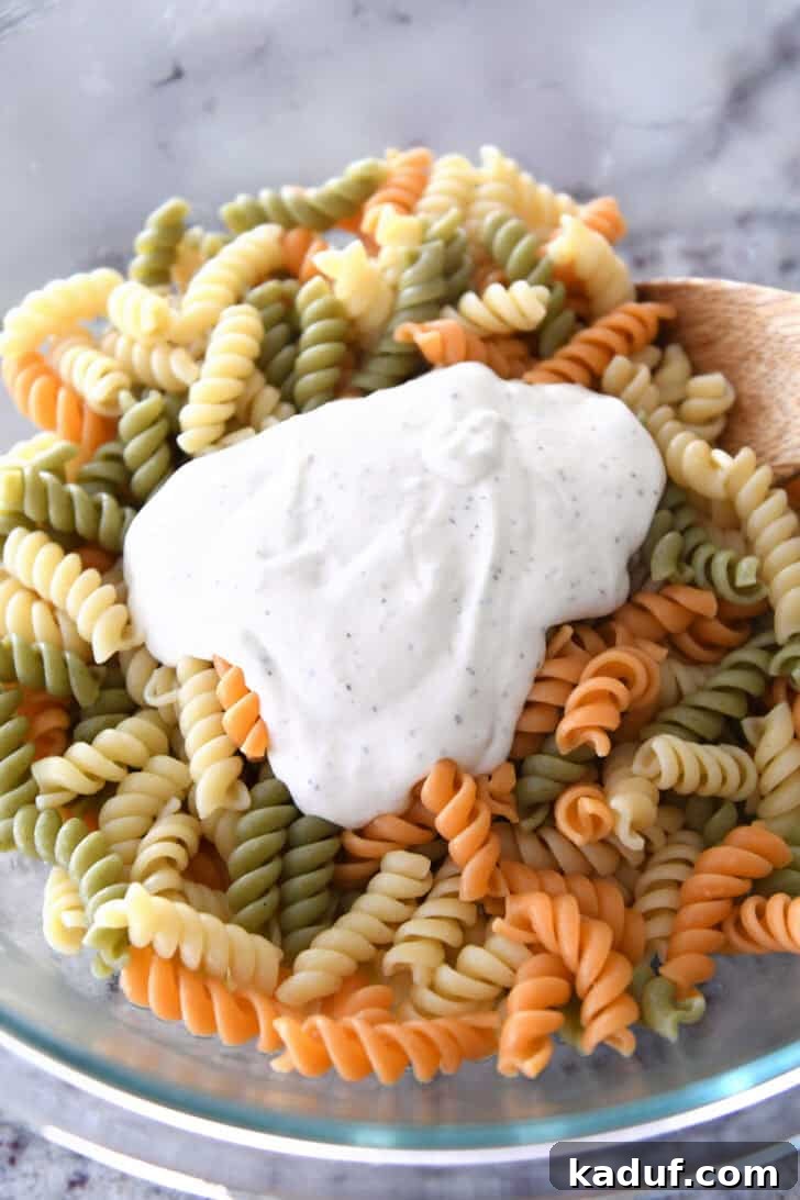 Vibrant Pasta Medley 3 A glass bowl with cooked tri-color rotini pasta, with a dollop of creamy Caesar dressing ready to be mixed in.