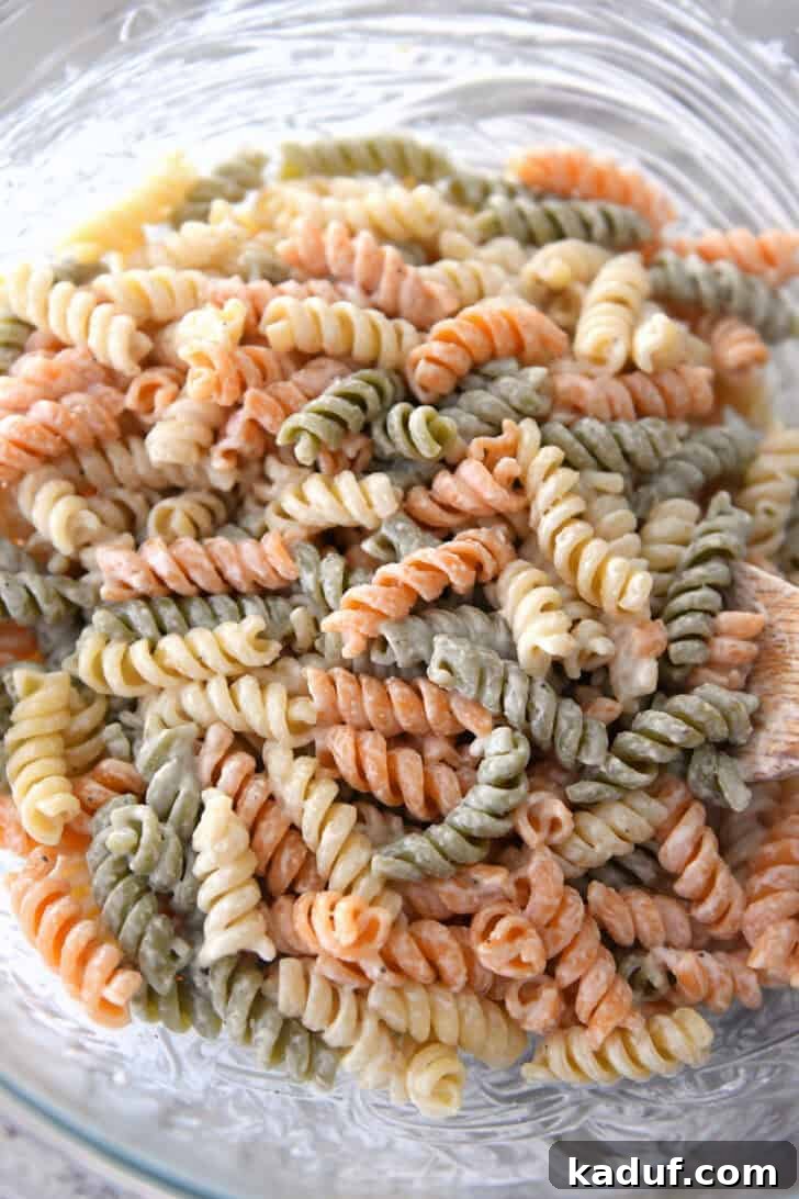 Vibrant Pasta Medley 4 Top-down view of tri-color rotini pasta thoroughly coated in Caesar dressing within a glass bowl.