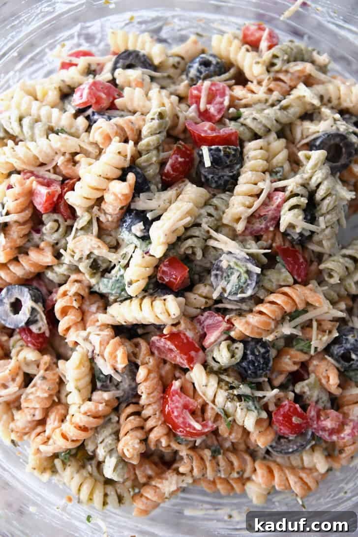 Vibrant Pasta Medley 6 Top-down view of tri-color rotini pasta mixed with dressing, olives, tomatoes, and parmesan cheese in a large glass bowl.