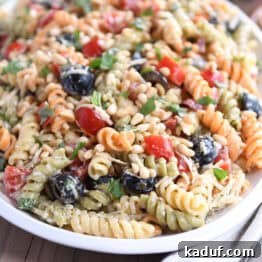 Pasta salad on oval white tray with olives, tomatoes, parmesan cheese and fresh basil.