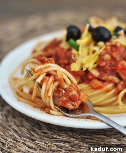 Chuck Wagon Pasta 2 A vibrant plate of Cowboy Spaghetti, featuring al dente noodles coated in a rich, reddish-brown sauce, generously topped with shredded cheese and black olives. The dish promises a hearty and flavorful experience.