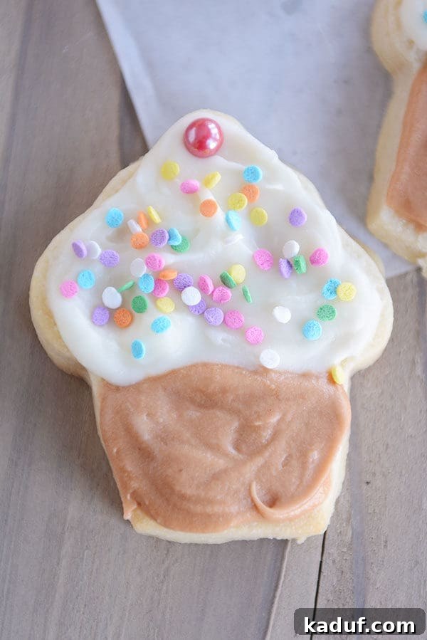 Velvet Cloud Sugar Cookies 5 A white sugar cookie decorated like a cupcake with a brown frosting on the bottom, and white frosting and sprinkles on the top of the cookie.