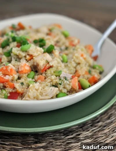 Vibrant Thai Chicken Quinoa Salad 3 White bowl with cooked quinoa salad filled with chicken, edamame, and peppers.