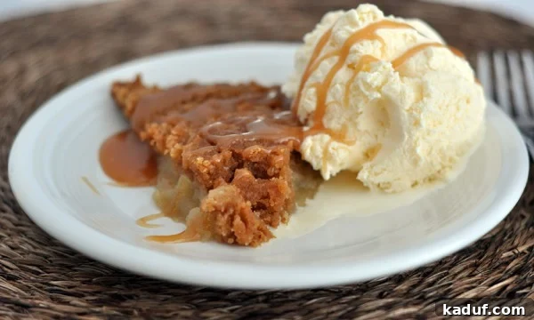 Gourmet Candy Apple Pie 2 A slice of golden-brown Candy Apple Pie with a scoop of melting vanilla ice cream and a drizzle of caramel sauce on a white plate, ready to be enjoyed.