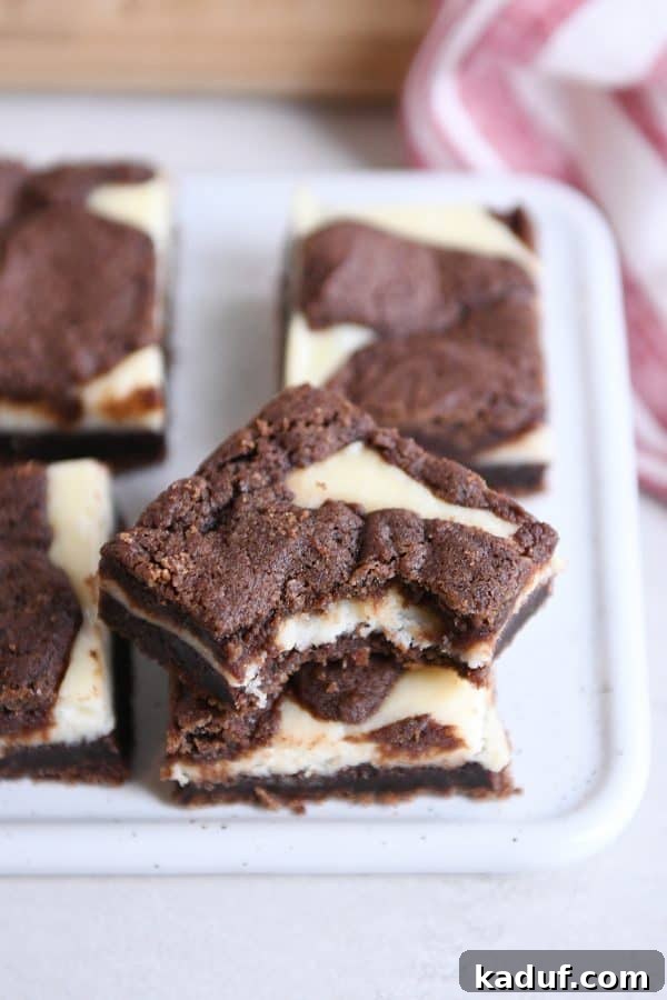 Zebra Cheesecake Brownies 2 Stack of black and white cheesecake brownies with a bite taken out of the top, showcasing the fudgy brownie and creamy cheesecake layers.