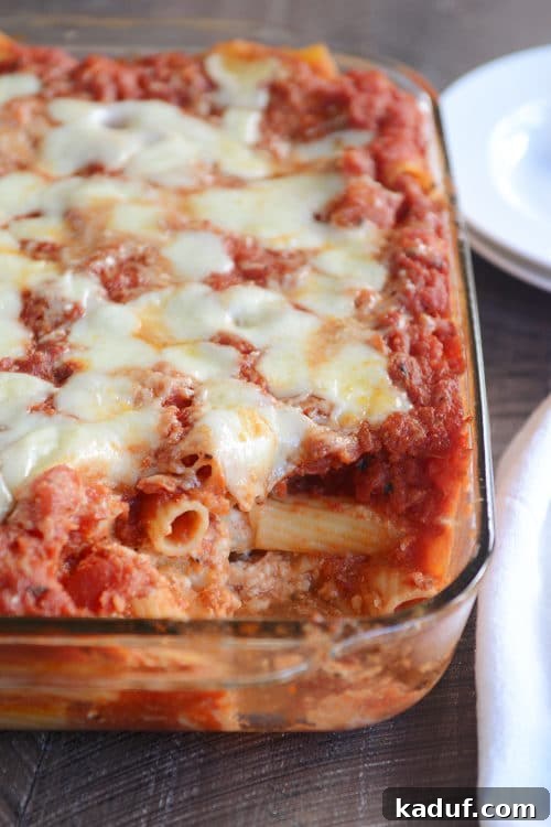 Homestyle Baked Ziti 2 A glass baking dish brimming with freshly baked ziti, a generous spoonful lifted out revealing layers of melted cheese, robust red sauce, and tender pasta.