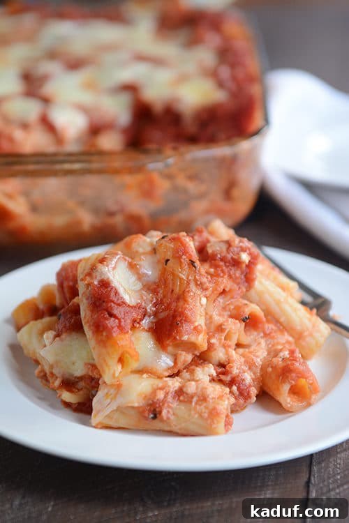 Homestyle Baked Ziti 4 A tantalizing scoop of baked ziti pasta, rich with melted mozzarella cheese and vibrant red sauce, presented beautifully on a white plate, ready to be enjoyed.