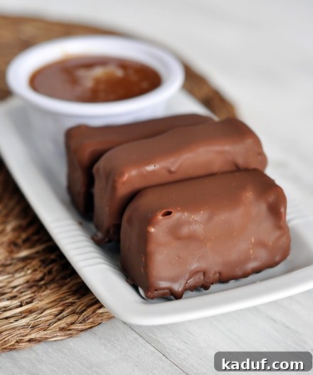 Decadent Polar Bars 4 Three chocolate-covered ice cream bars neatly arranged on a white platter, accompanied by a small bowl of warm caramel sauce, ready for dipping.