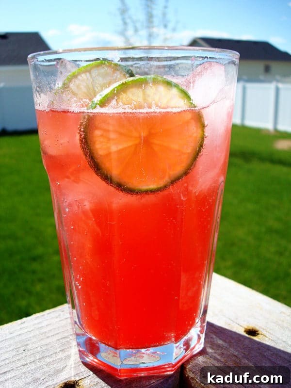Crimson Zest Sparkler 3 A tall glass filled with the vibrant raspberry lime drink, adorned with lime wedges and plenty of ice.