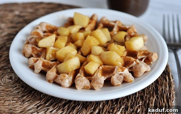 Golden Apple Cinnamon Waffles with Spiced Syrup 2 A white plate featuring a golden waffle generously topped with cooked apple chunks and glistening cinnamon sauce. Perfect for a cozy breakfast.