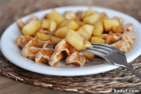 Golden Apple Cinnamon Waffles with Spiced Syrup 3 Close-up shot of an apple cinnamon waffle on a pristine white plate, showcasing the rich cinnamon topping and apple pieces.