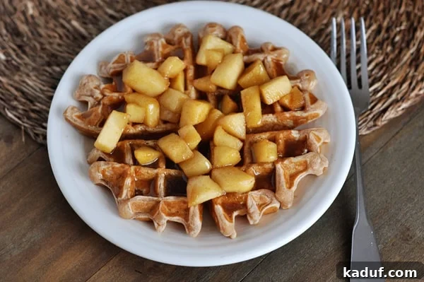 Golden Apple Cinnamon Waffles with Spiced Syrup 4 An overhead view of a golden waffle topped with caramelized apples and a generous drizzle of cinnamon syrup on a white plate.