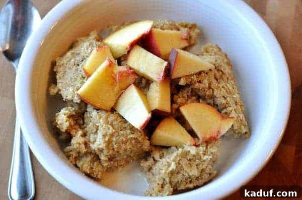 Golden Oat Bake 2 A white bowl filled with baked oatmeal, drizzled with milk and topped with fresh peach chunks.