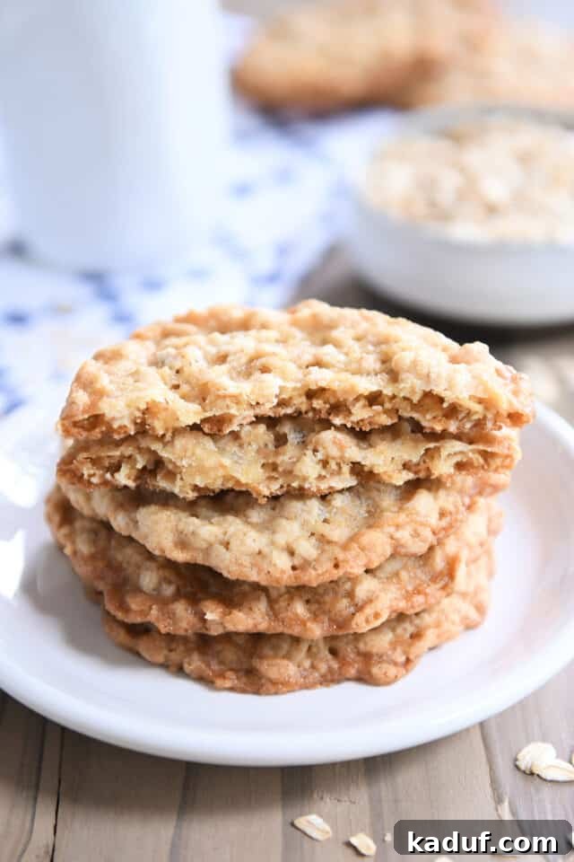 Chewy Oatmeal Lace Cookies 5 Four thin oatmeal cookies on white plate with top cookie broken in half.