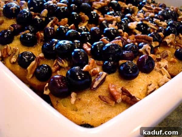 Baked Blueberry Pecan French Toast with Fresh Berries A tantalizing close-up of baked blueberry pecan french toast, golden brown and topped with plump, juicy blueberries and toasted pecans, in a white baking dish.