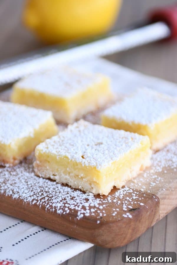Zingy Lemon Bar Perfection 2 Lemon bars on a cutting board, generously sprinkled with powdered sugar, showcasing their irresistible appeal.