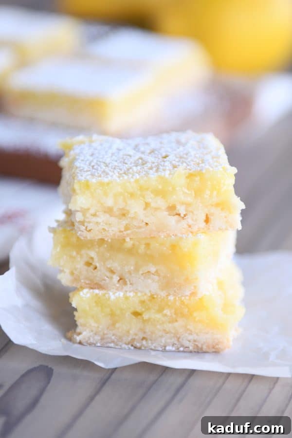 Zingy Lemon Bar Perfection 3 Three golden-yellow lemon bars elegantly stacked on top of each other, highlighting their thick filling and crisp crust.