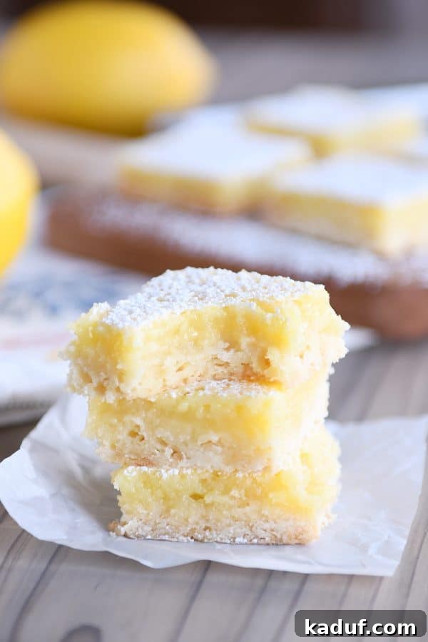 Zingy Lemon Bar Perfection 4 A stack of the best lemon bars, with a bite taken out of the top bar, revealing the creamy lemon filling and crumbly crust.