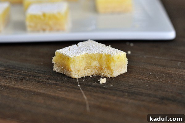 Zingy Lemon Bar Perfection 6 A perfectly cut square of lemon bar with a small bite taken out, highlighting its rich texture and bright color.