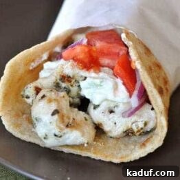 A small plate of chicken gyros with tzatziki sauce and fresh vegetables.