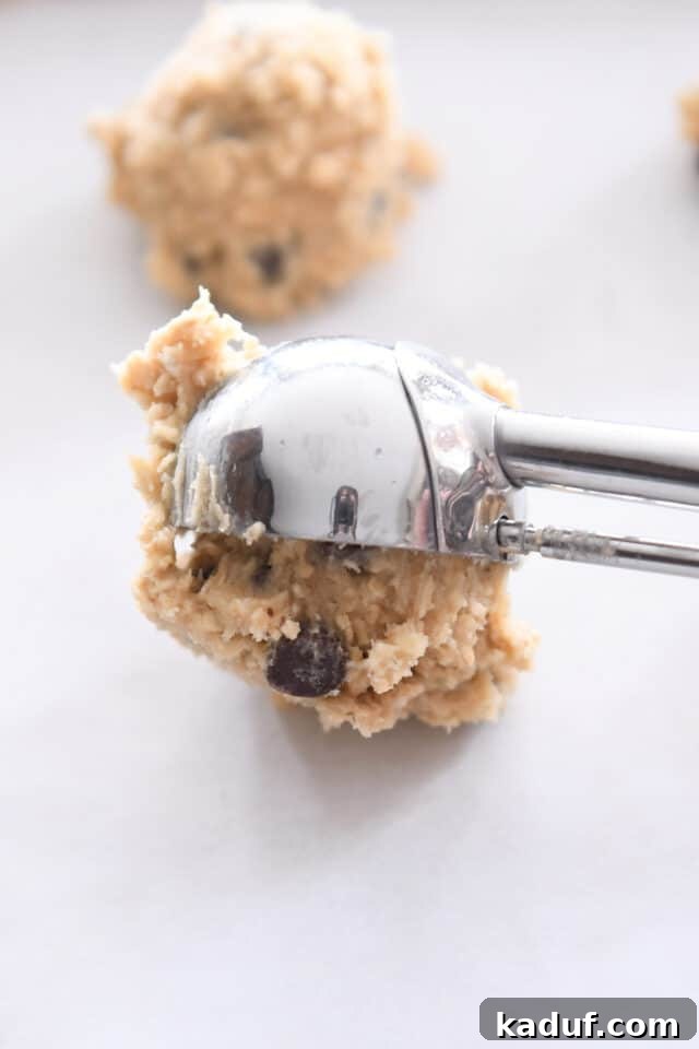 Chewy Oatmeal Chocolate Chip Cookies 5 A cookie scoop forming a ball of oatmeal chocolate chip cookie dough onto a parchment-lined baking sheet.