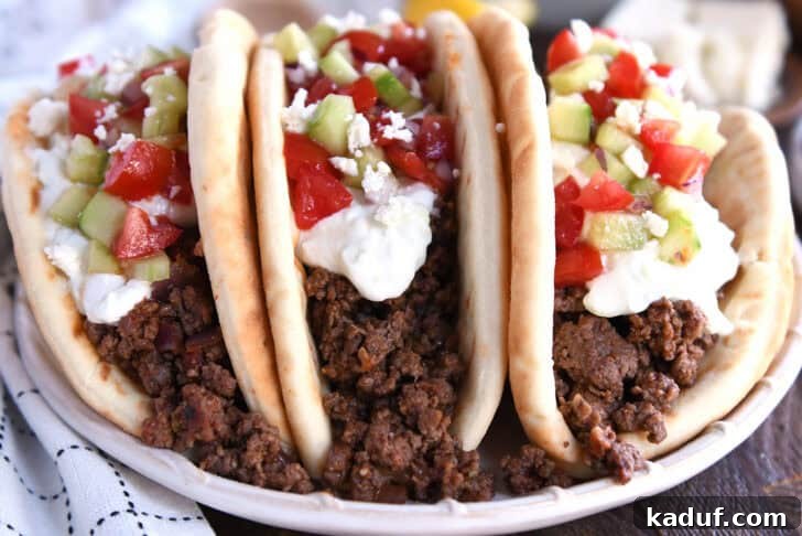 Epic Greek Tacos 3 Front view of three stuffed greek flatbread tacos topped with tzatziki sauce, chopped cucumbers, and diced tomatoes.