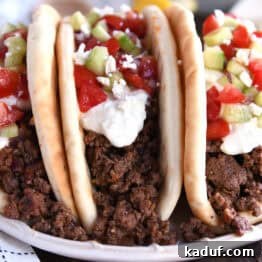 Front view of three stuffed greek flatbread tacos topped with tzatziki sauce, chopped cucumbers, and diced tomatoes.