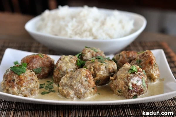 Vibrant Thai Green Curry Meatballs 2 White dish with browned meatballs covered in sauce and parsley and a dish of cooked white rice behind it.
