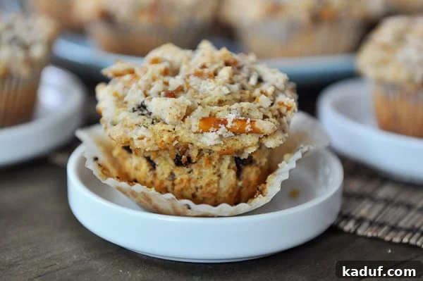 Salty Sweet Pretzel Chocolate Chip Muffins 2 A golden-brown pretzel-crusted chocolate chip muffin on a small white plate, showcasing its rich texture and generous chocolate chips.