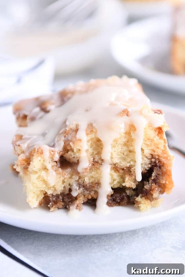 Indulgent Cinnamon Swirl Cake 2 A square slice of cinnamon roll cake with luscious glaze drizzling down its sides, on a white plate.