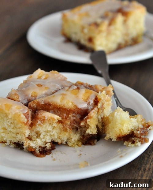 Indulgent Cinnamon Swirl Cake 10 A white plate featuring a generous piece of cinnamon roll cake with a bite taken out, highlighting its moist interior and perfect glaze.