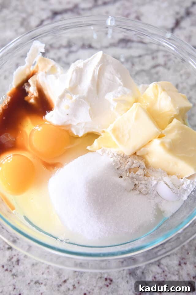 Indulgent Cinnamon Swirl Cake 3 All the cake ingredients – butter, flour, sugar, eggs, vanilla, sour cream, and baking powder – gathered in a clear glass mixing bowl, ready to be combined.