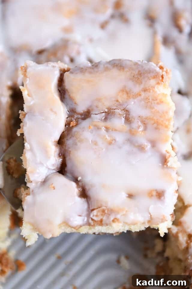 Indulgent Cinnamon Swirl Cake 7 A delectable piece of glazed cinnamon roll cake being lifted off the pan with a spatula, showcasing its warm, inviting appeal.