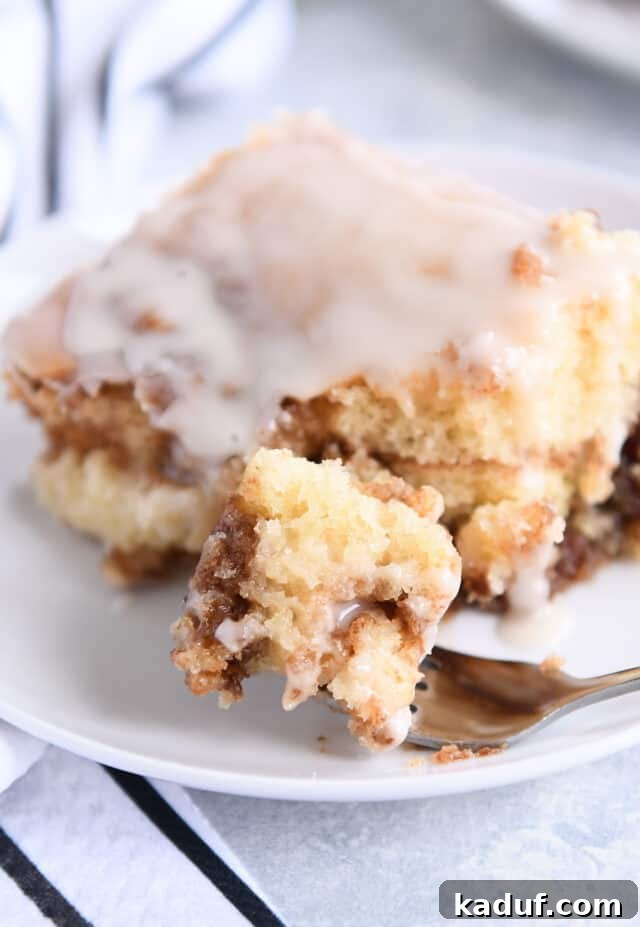 Indulgent Cinnamon Swirl Cake 8 A close-up of a bite of cinnamon roll cake on a fork, resting on a white plate, highlighting its moist texture and cinnamon swirls.