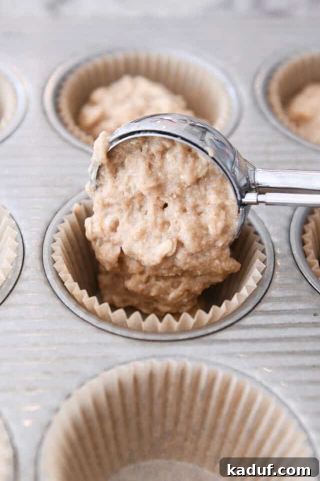 Wholesome Apple Oat Muffins 4 A scoop of applesauce oat muffin batter being placed into a lined muffin tin, ready for baking. The batter appears thick and wholesome, studded with oats.