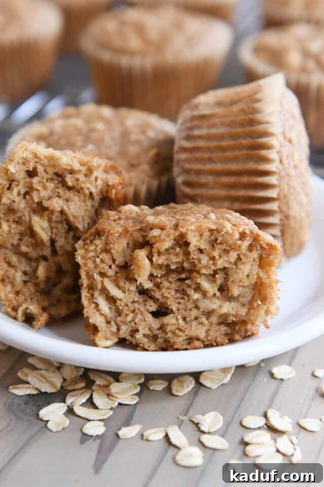 Wholesome Apple Oat Muffins 5 Several healthy applesauce oat muffins arranged on a white plate, with one muffin split in half to reveal its soft, textured interior filled with oats.