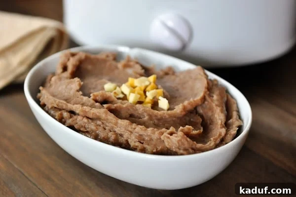Fat-Free Slow Cooker Refried Beans 2 White oval dish full of refried beans in front of a slow cooker.