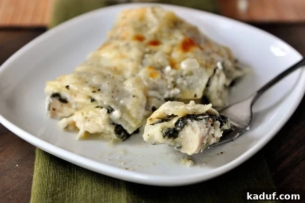 Creamy Chicken and Spinach Lasagna 2 A perfectly portioned slice of White Chicken and Spinach Lasagna on a white plate, with a fork poised for a bite, showcasing the creamy layers of chicken, spinach, and pasta.