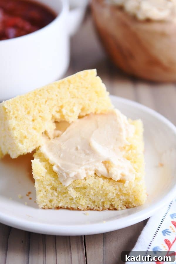 The Ultimate Cornbread with Cloudlike Honey Butter 2 A golden-brown slice of cornbread, split in half to reveal its fluffy texture, served alongside whipped honey butter.